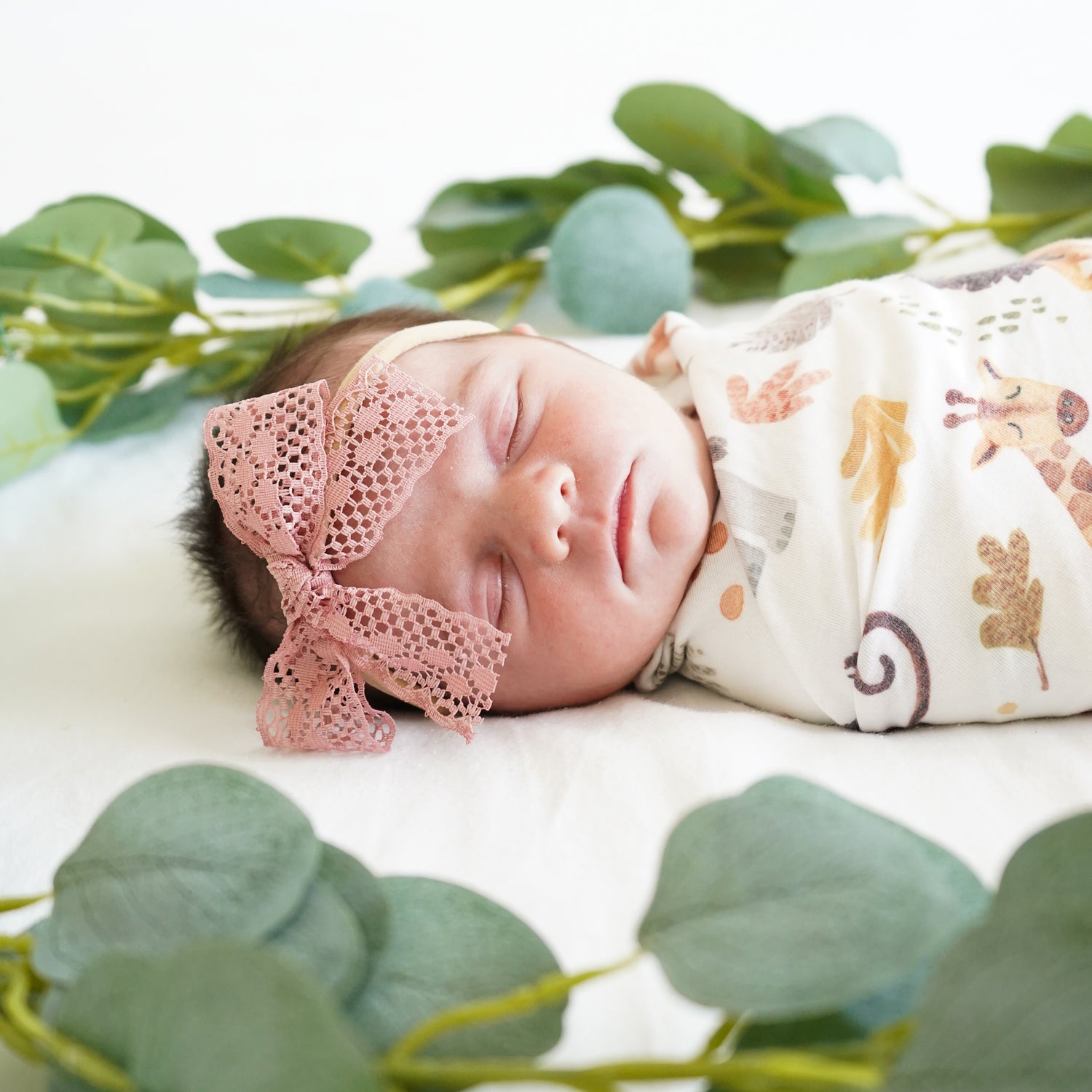 baby in eucalyptus wrapped in safari animals swaddle wearing stretchy headband pink lace bow