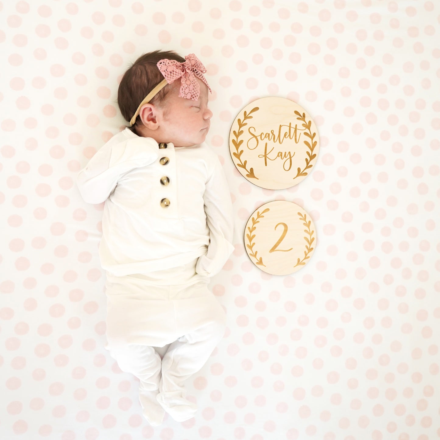 baby in pajamas on pink swaddle with 2 month wood engraved sign and pink bow