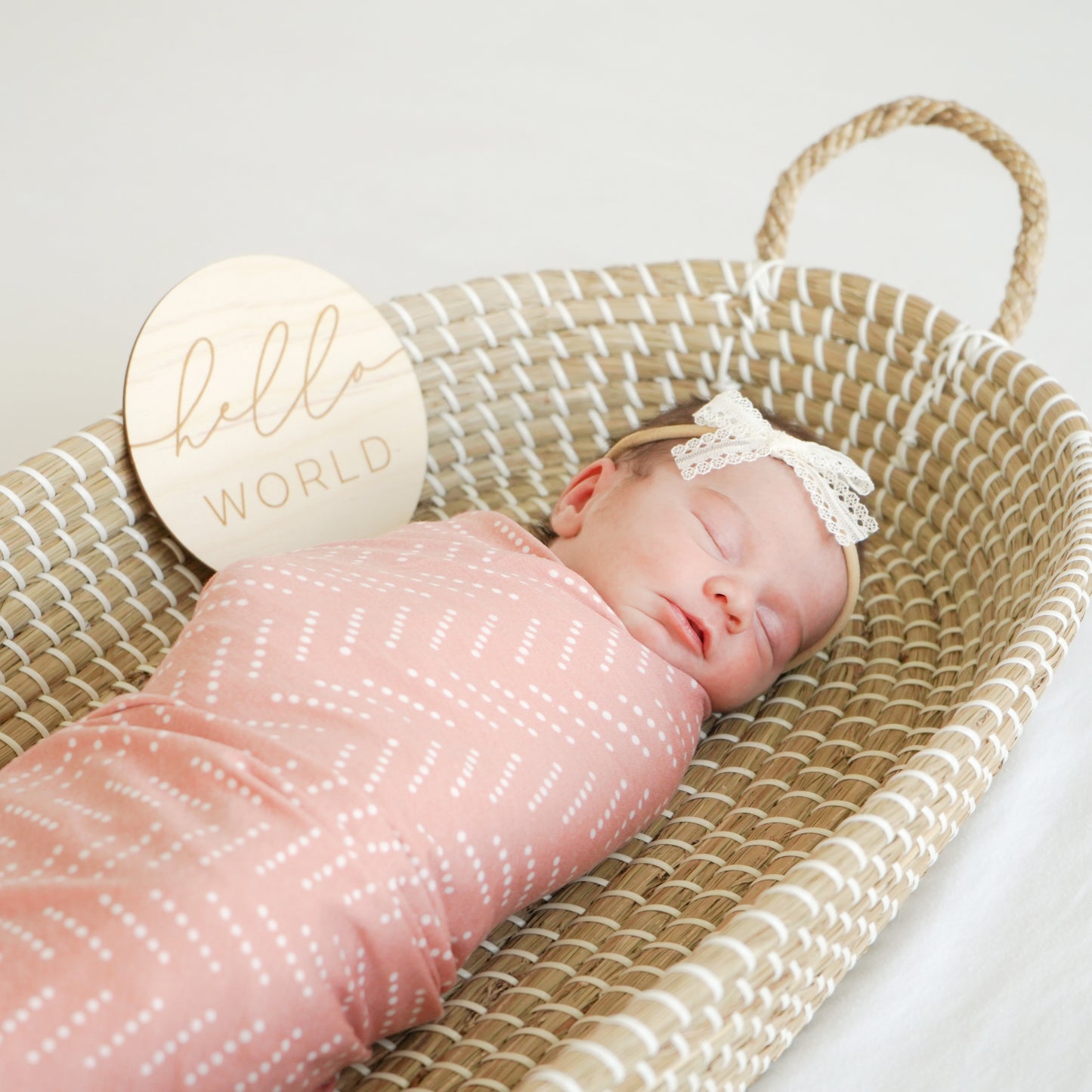 baby with desert dots swaddle and hello world sign and lace bow