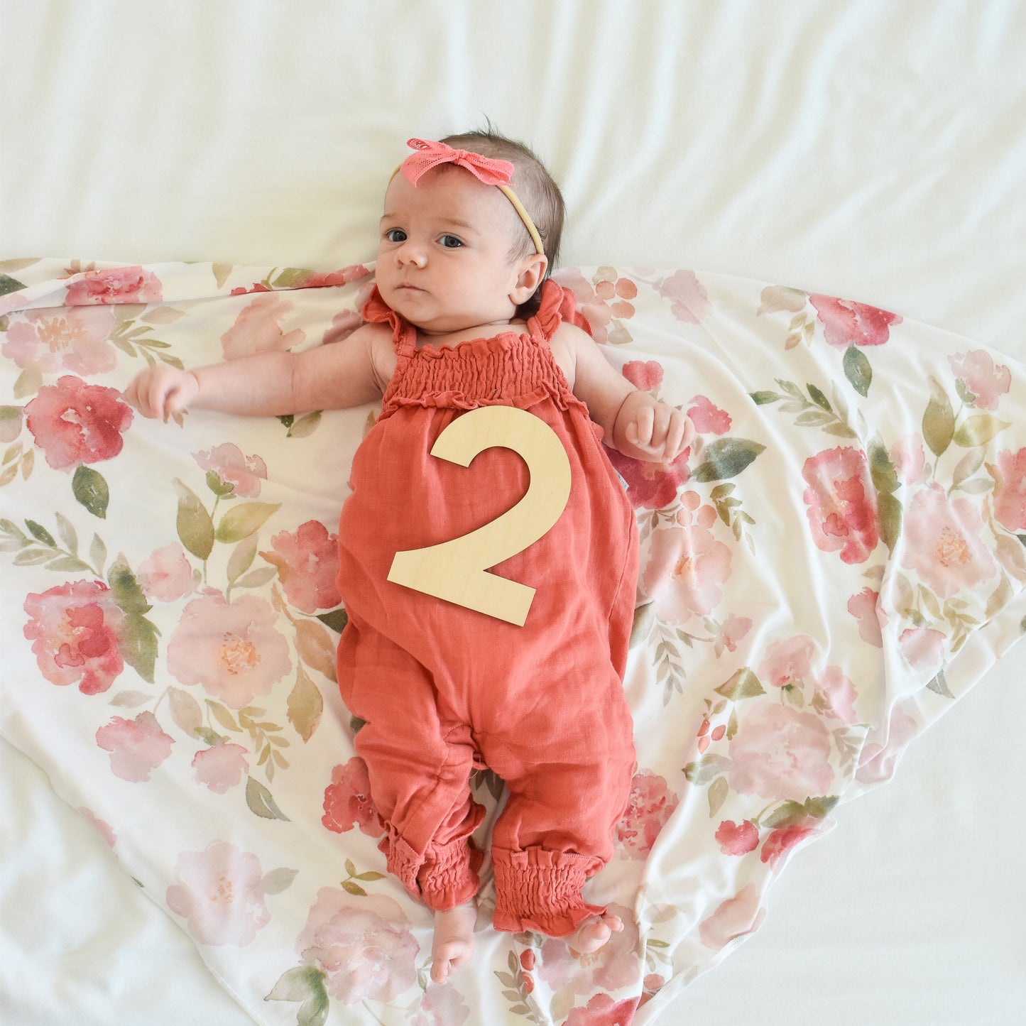 two month old baby with wooden sign and coral pink bow headband village