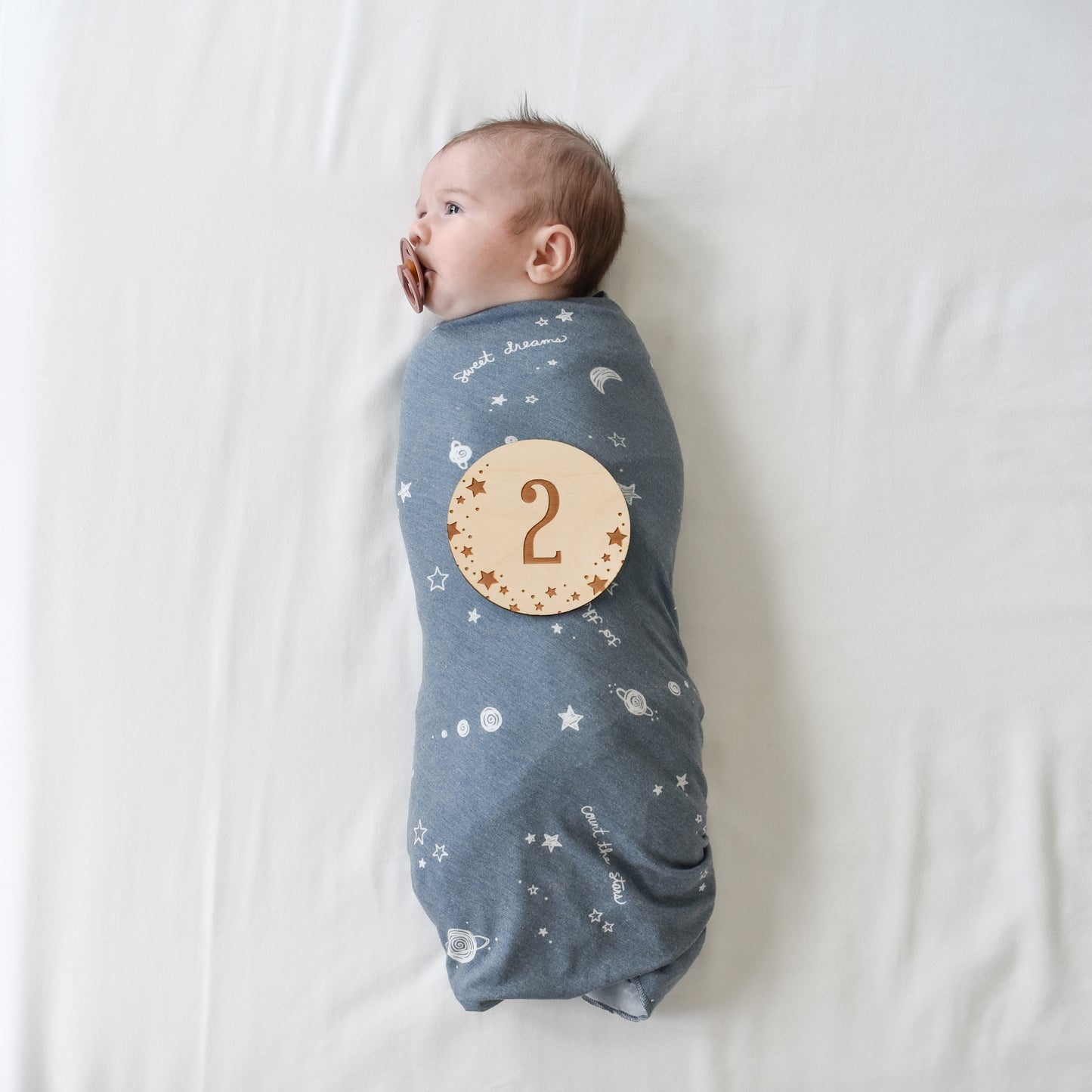 baby with pacifier and swaddle blanket with number 2 wooden disc sign plaque