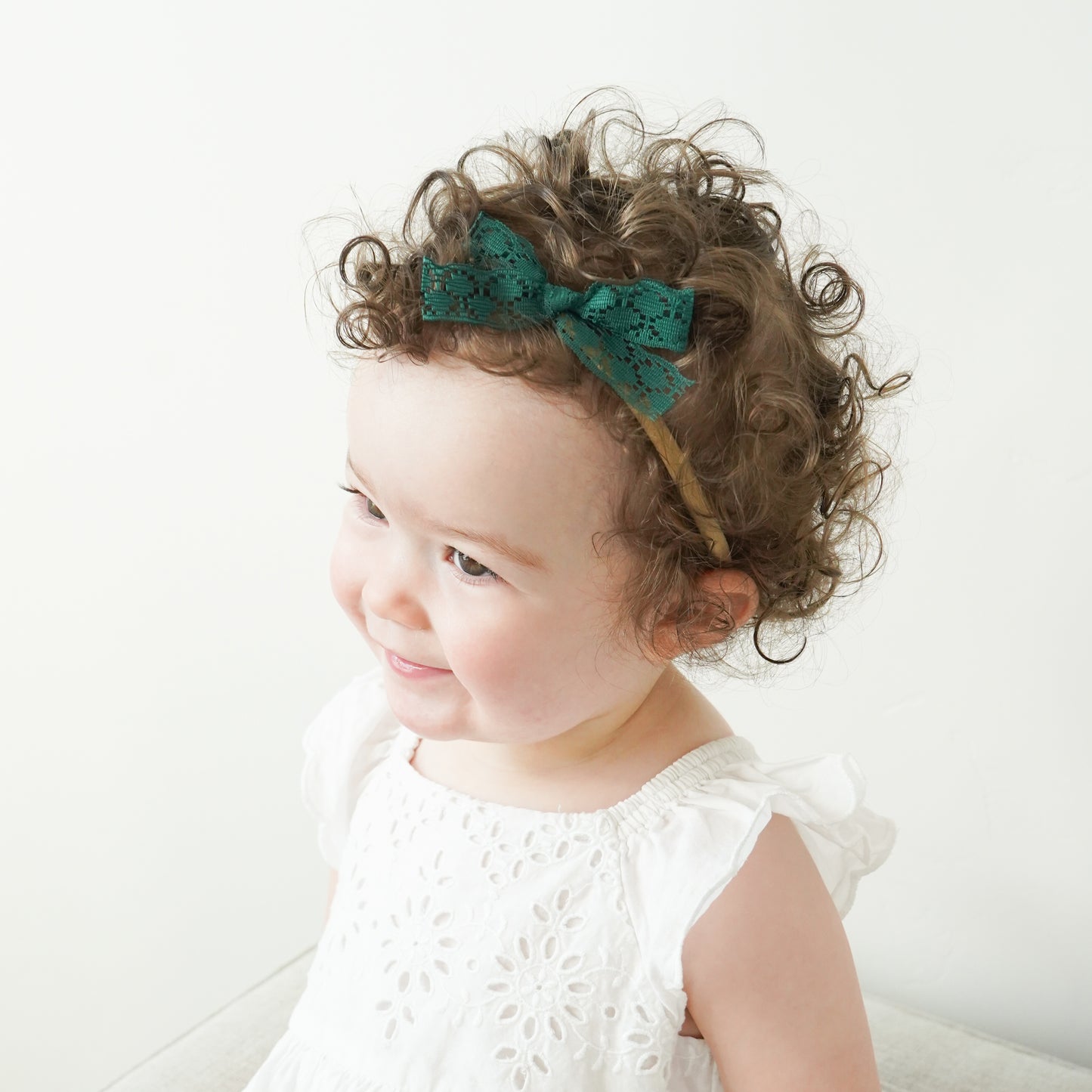 curly haired toddler wearing olivia headband with emerald green lace bow
