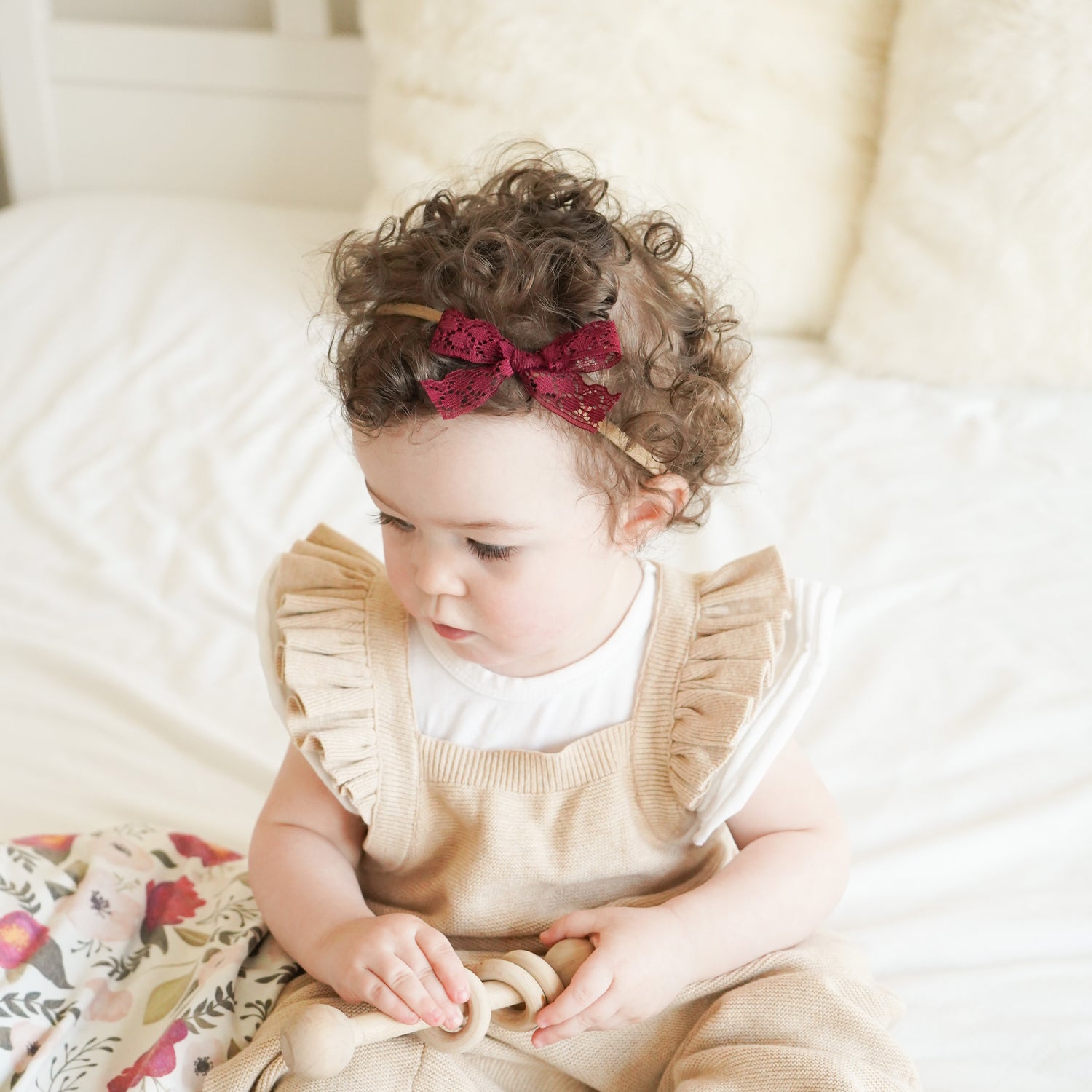 baby on bed wearing headband with swaddle and wood baby toy village baby shop