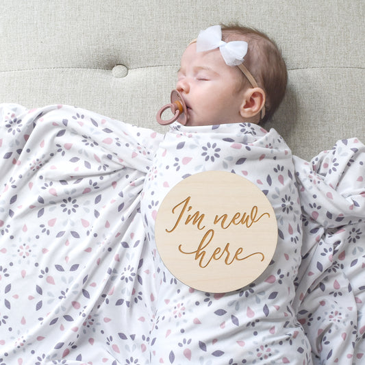 baby girl in swaddle and bow with wood sign for newborn photography
