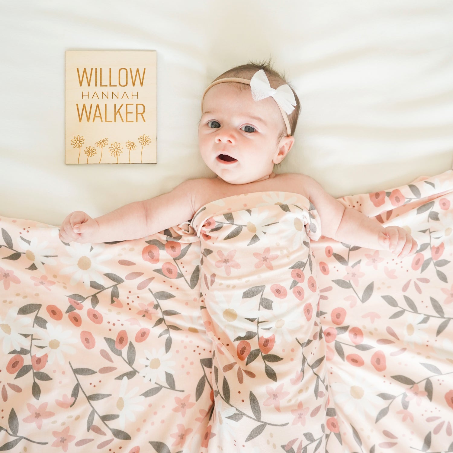baby girl with custom daisy name sign and peach posey swaddle blanket