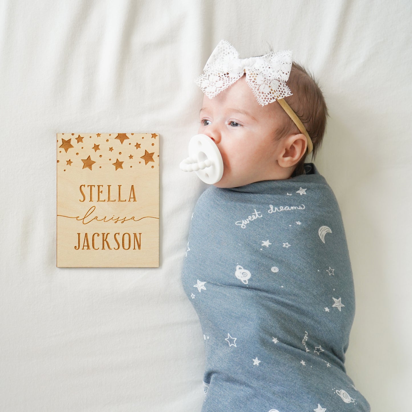 Baby girl with white lace Lily bow, white bibs pacifier, starry dreams swaddle and custom name sign