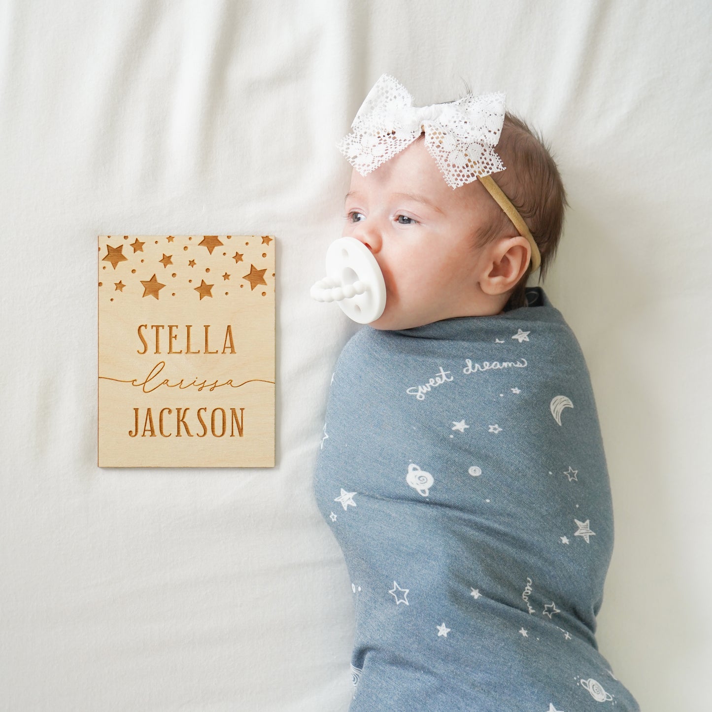 baby girl with custom wooden name sign, bibs, pacifier, blue stars blanket