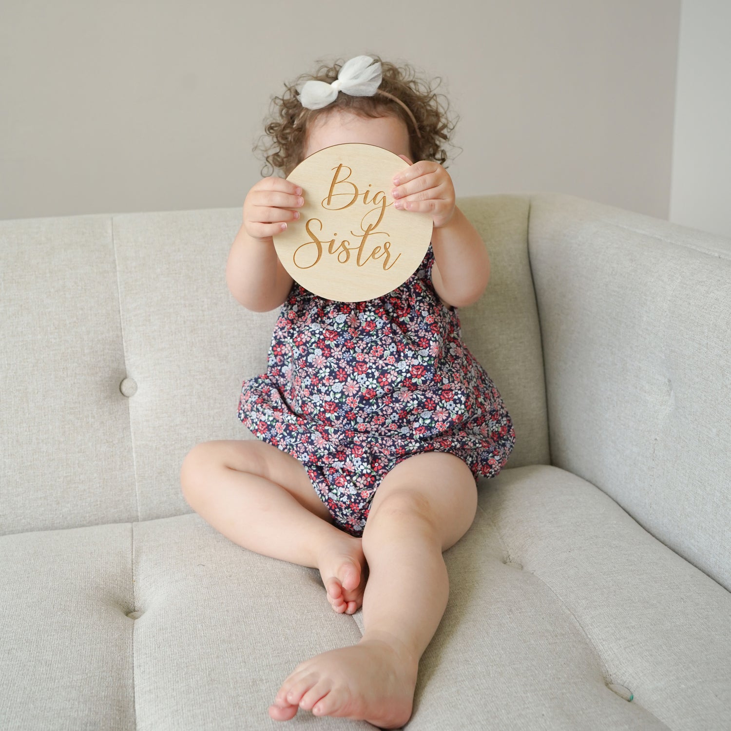 toddler girl holding big sister sign in front of her face to announce baby pregnancy