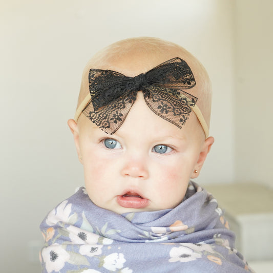 baby girl in village baby swaddle and cute hair bow accessory black raven lace