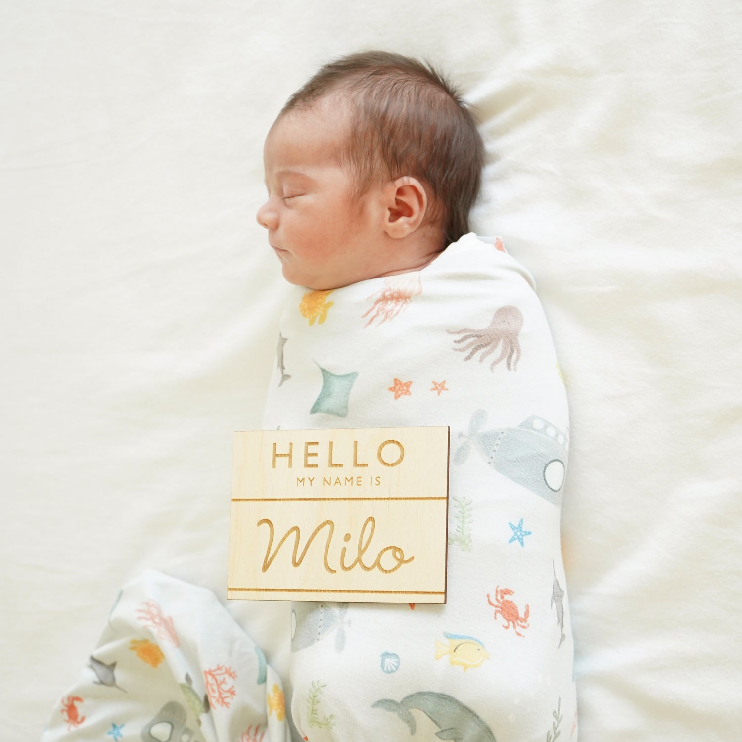 baby in underwater swaddle with name badge style sign hello my name is