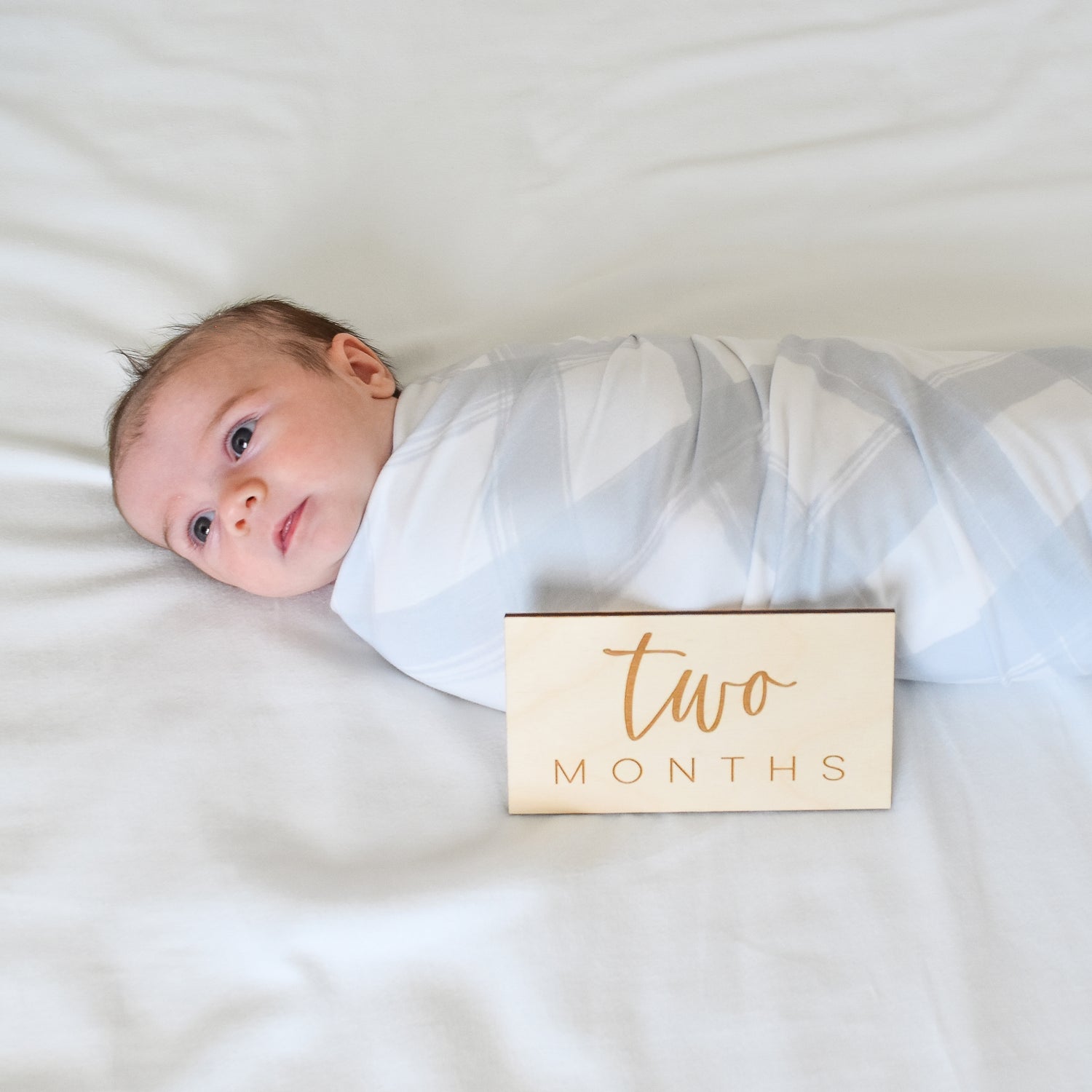 baby in swaddle in bed with two months wood sign gift