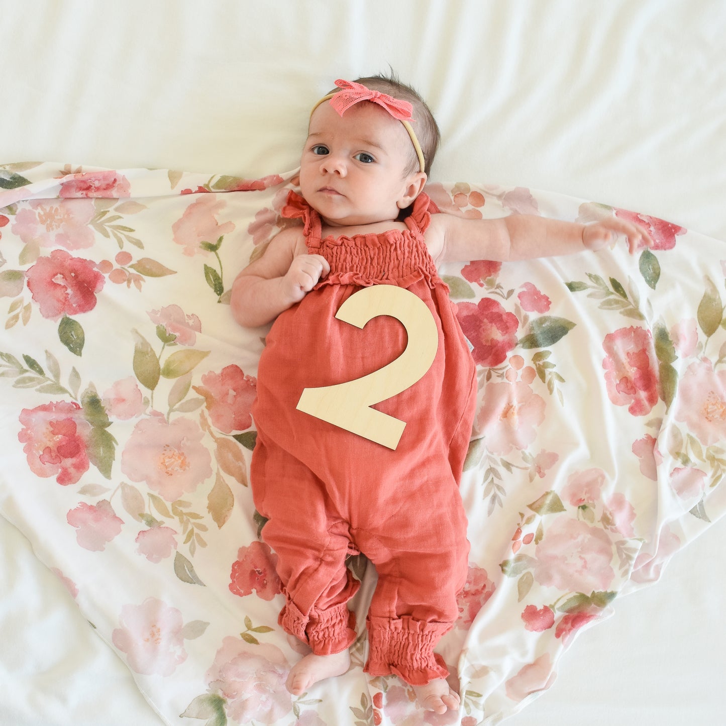 cute baby girl with number two sign because she is two months old with floral swaddle knit blanket