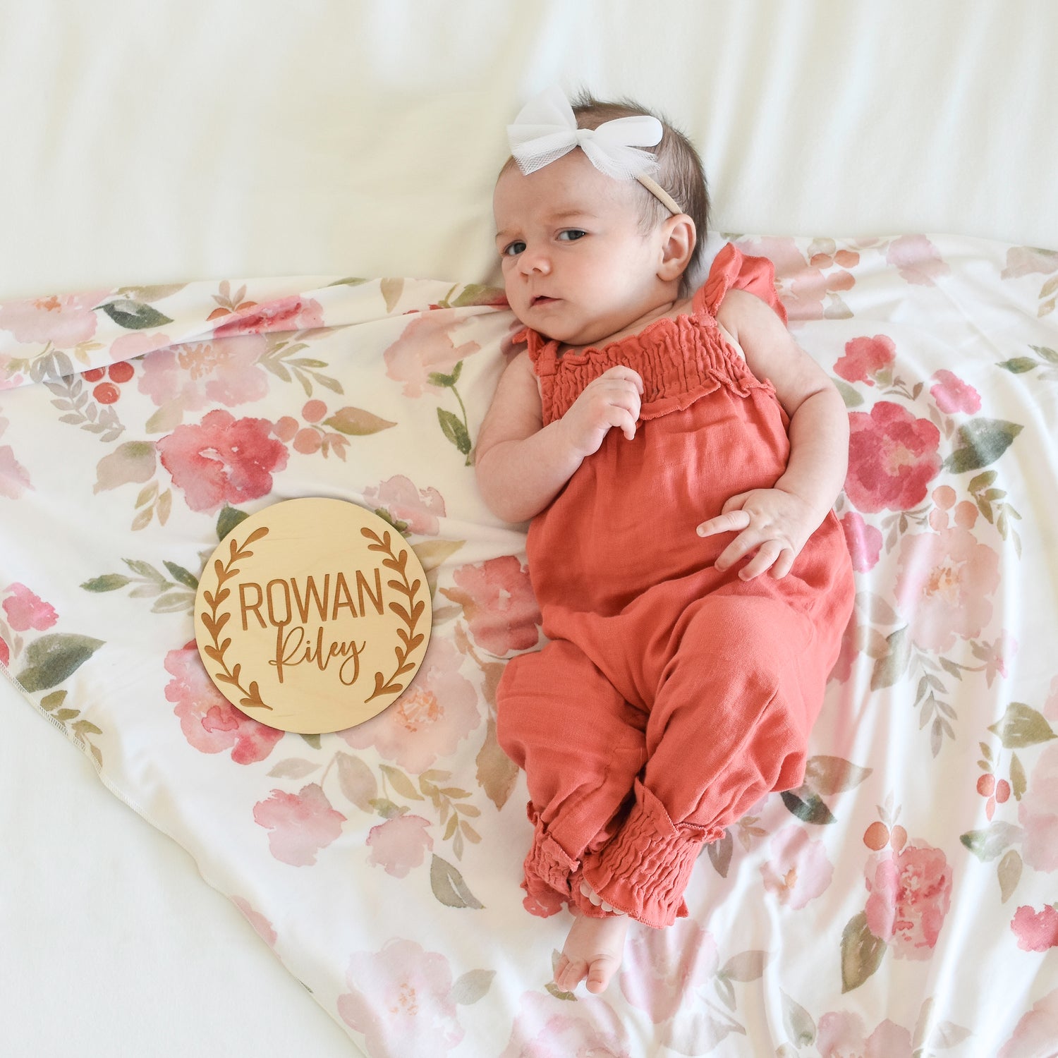 baby in jumpsuit with floral swaddle, tulle bow and custom name sign announcement