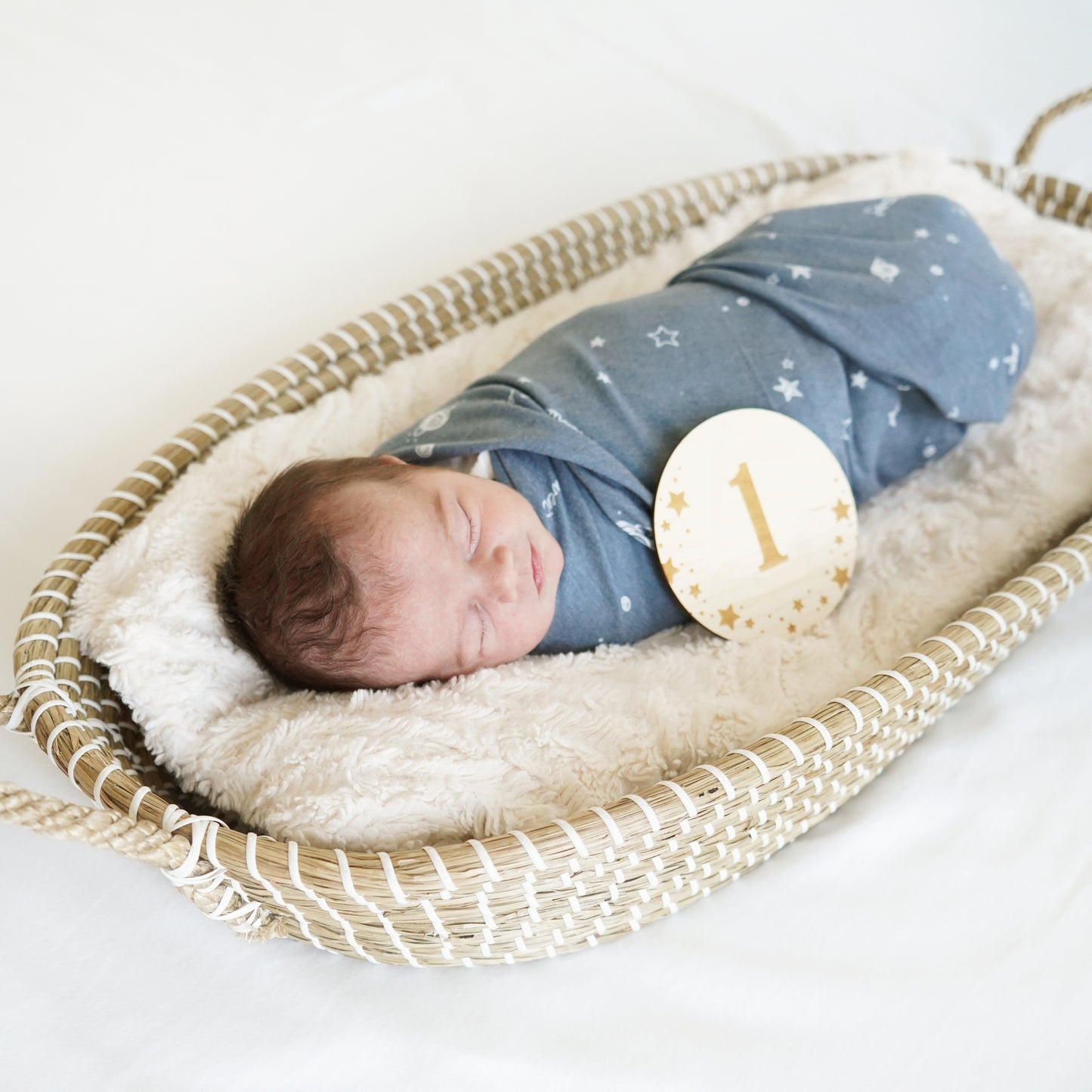 baby in starry dreams swaddle in basket with number one wooden sign