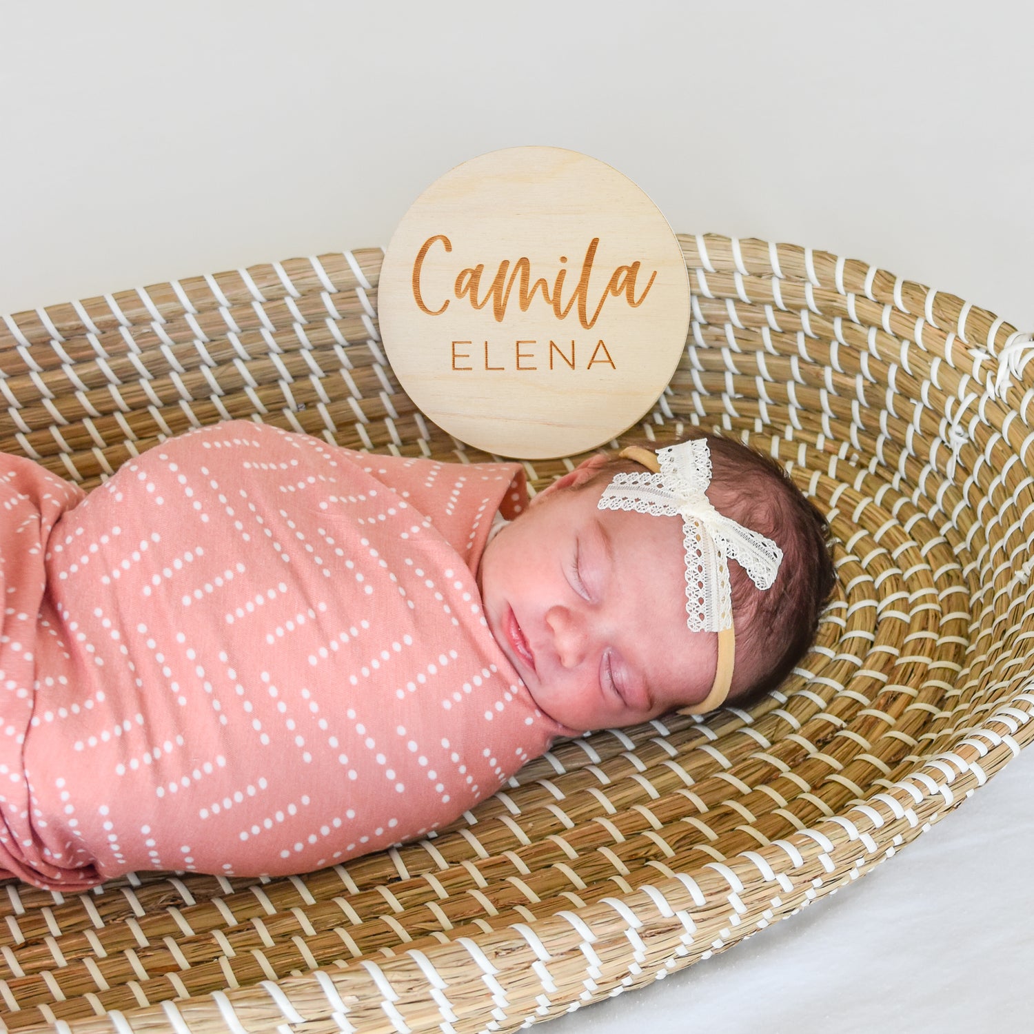 baby girl in swaddle and bow in basket with name sign photo